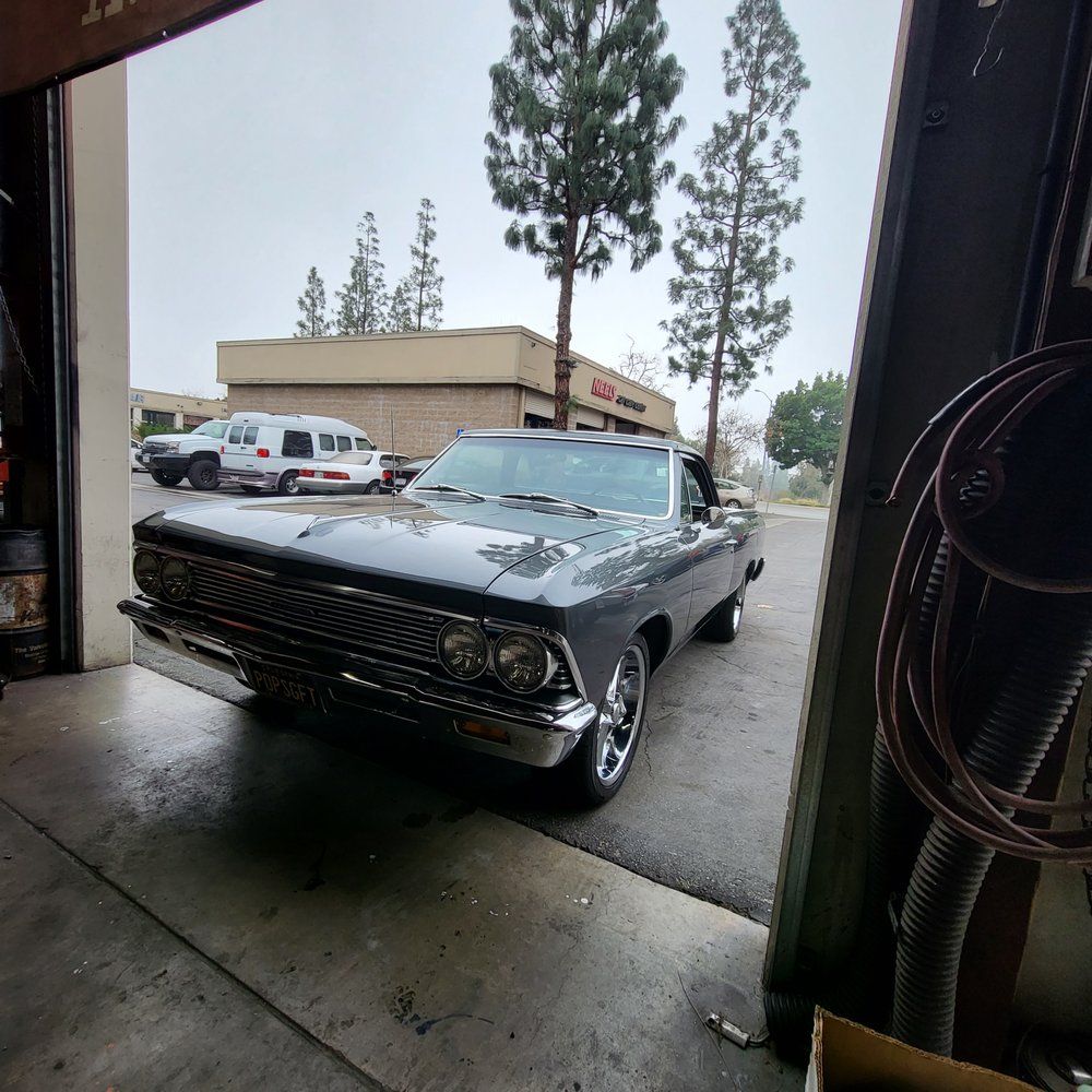 A black car is parked in a garage with trees in the background