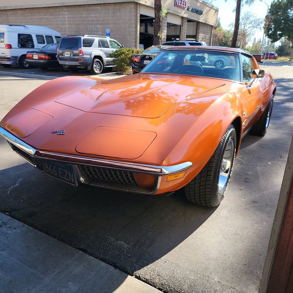An orange corvette is parked on the side of the road