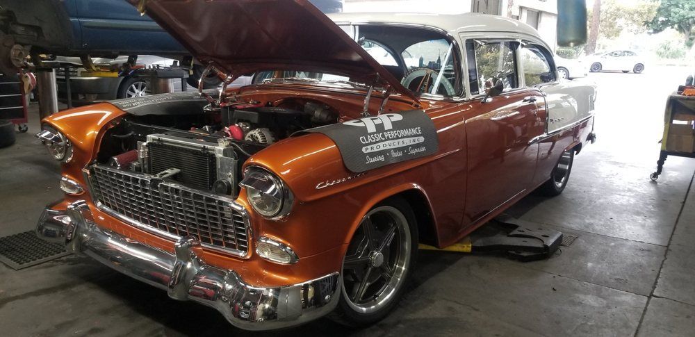 An old car with the hood up is sitting in a garage.