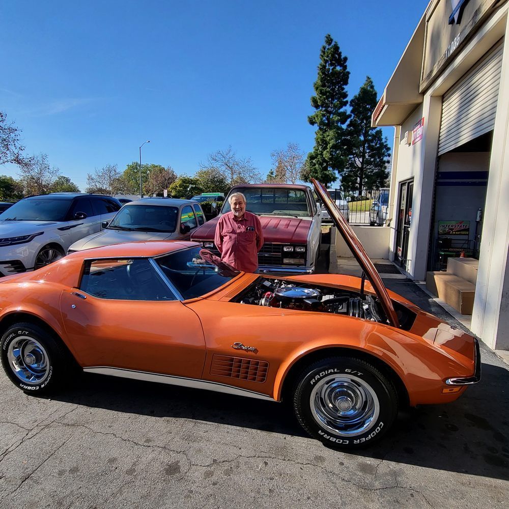 A man is standing next to an orange corvette with the hood open