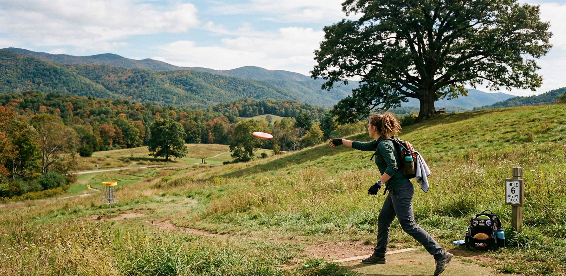 A disc golfer throwing a disc on a scenic mountain course with trees and hills in the distance.