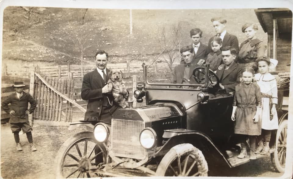 A vintage black-and-white photo of a group posing with a Model T car in a rural setting.