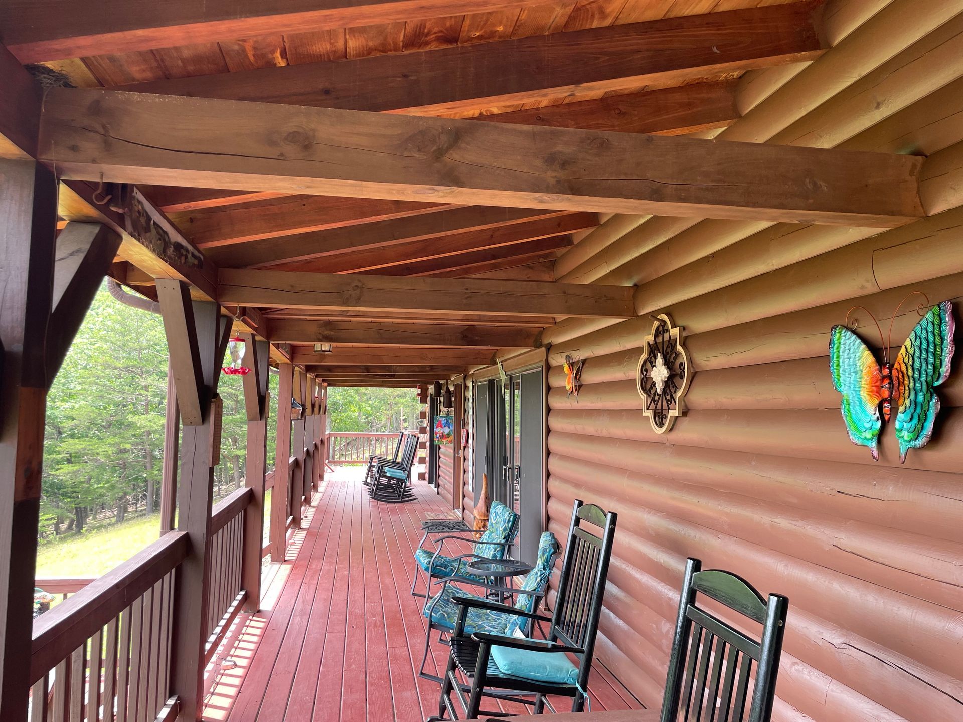 A wooden deck of a log cabin with rocking chairs, a decorative metal butterfly, and an outdoor view of trees.