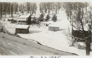 A black-and-white landscape of several small buildings and scattered trees covered in deep snow, dated November 20, 1925.