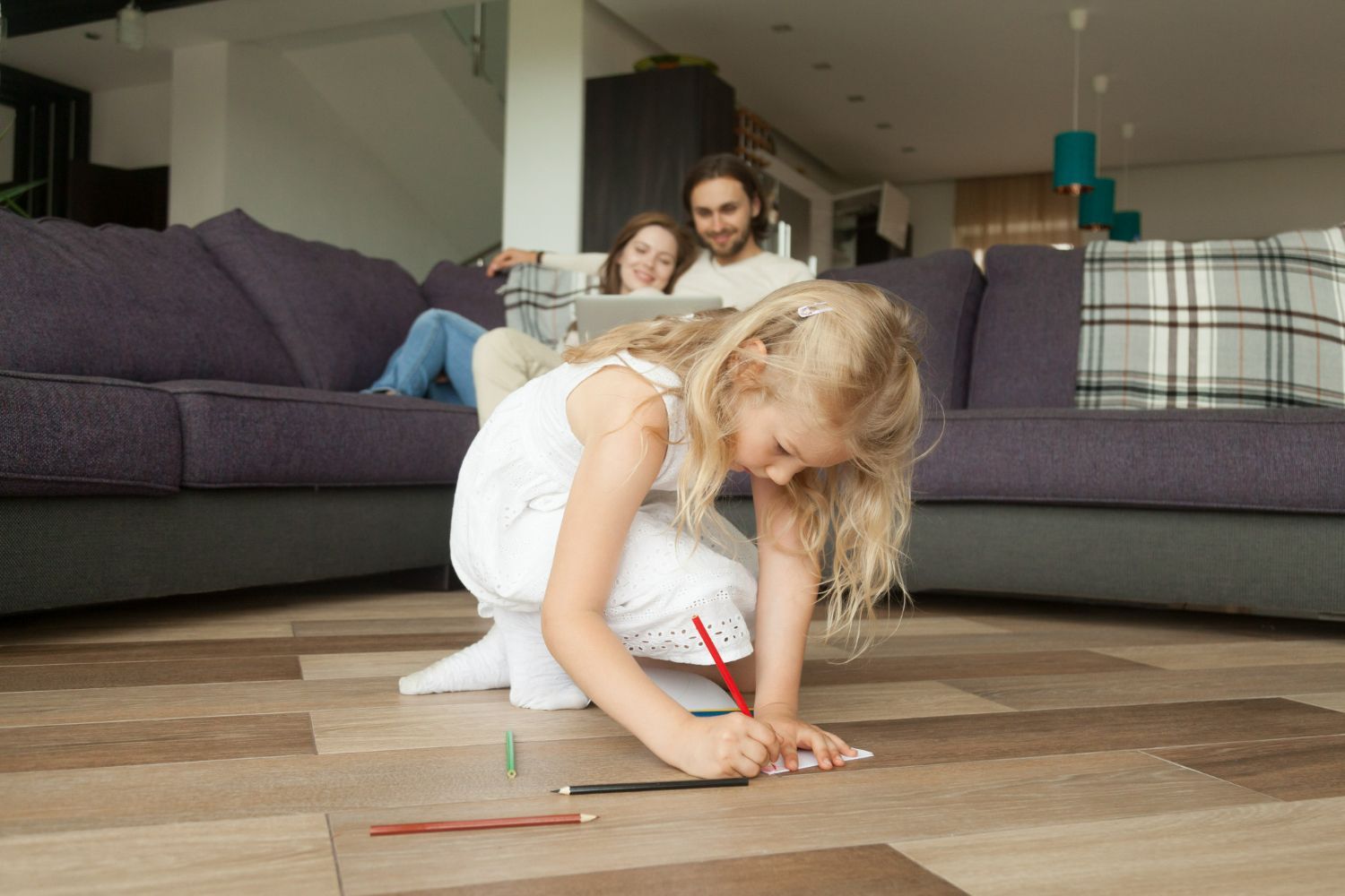 Girl drawing on the floor; parents on the couch in the background.