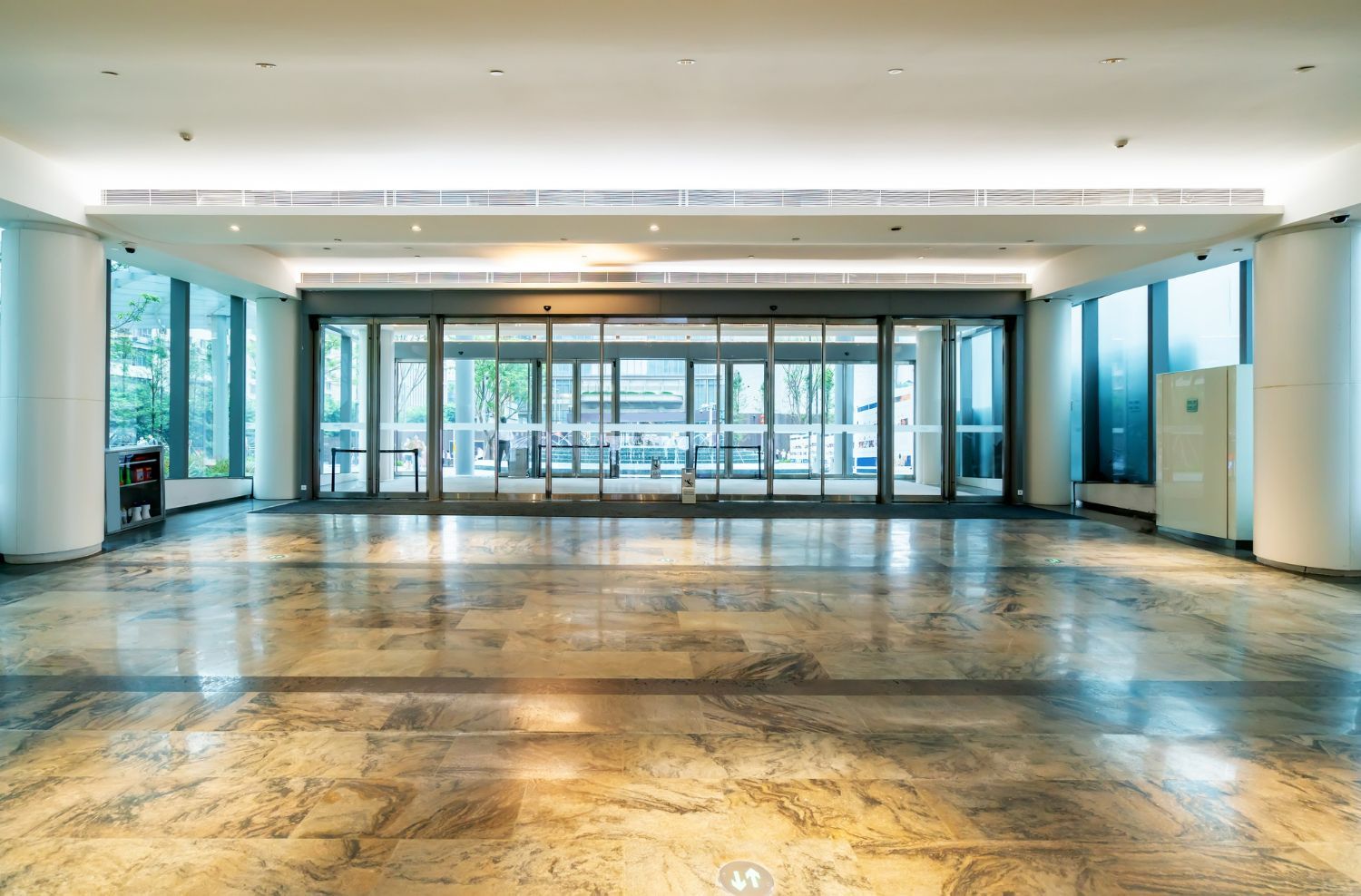 Empty, bright lobby with automatic glass doors, marble floor, and recessed lighting.