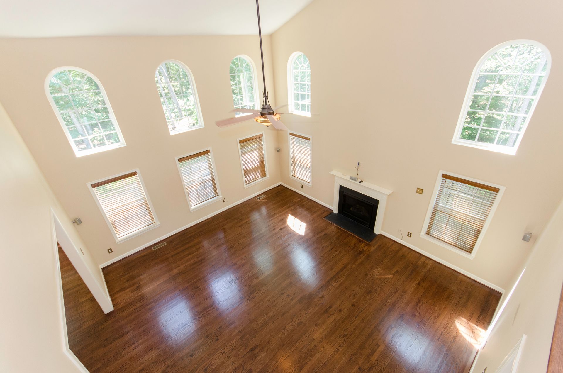 High-angle view of a living room with arched windows, fireplace, dark wood floors, and a ceiling fan.