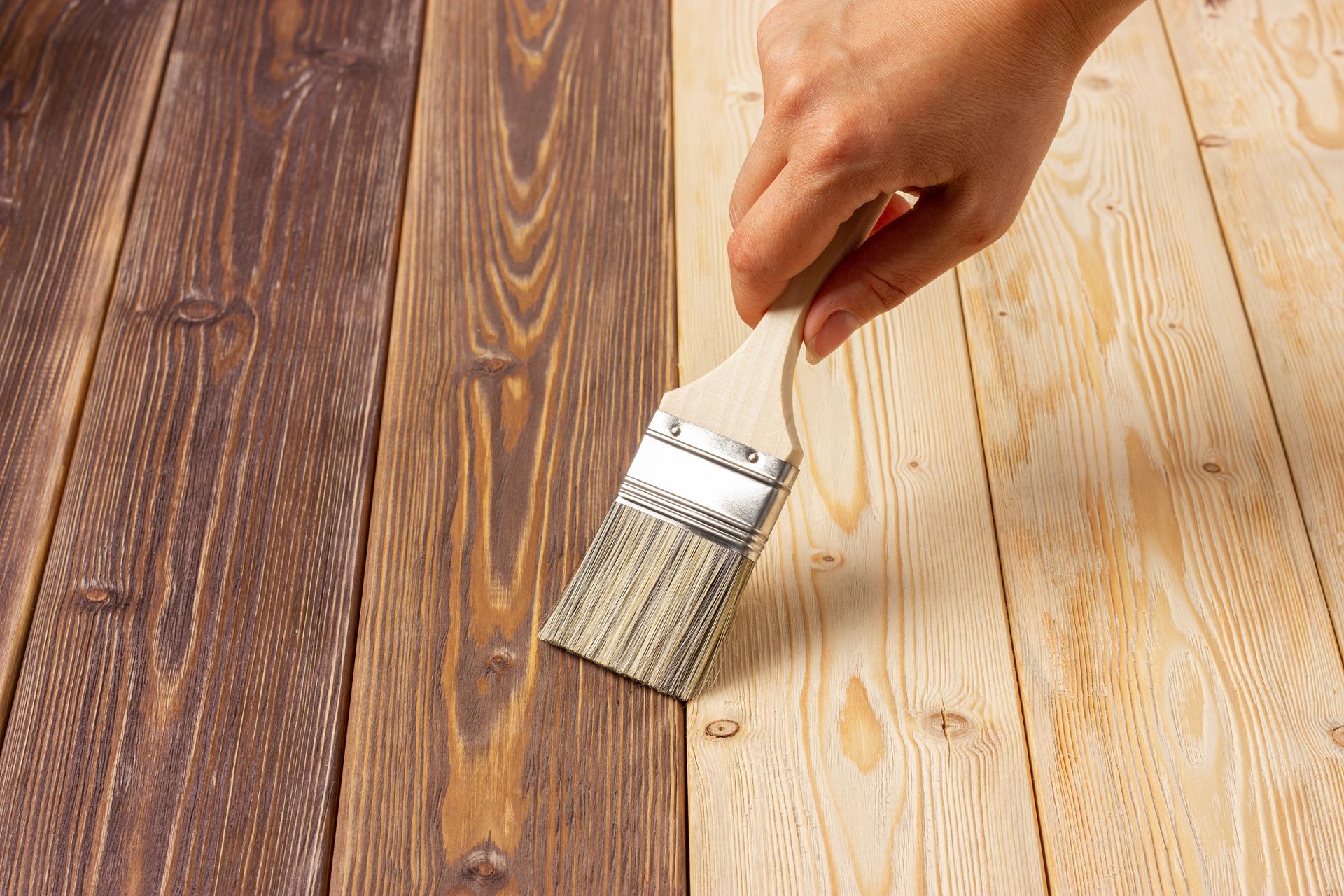 A person is painting a wooden floor with a brush.