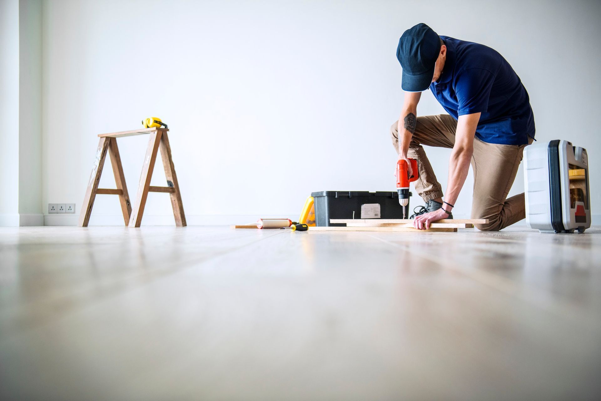 A man is kneeling on the floor working on a piece of wood.