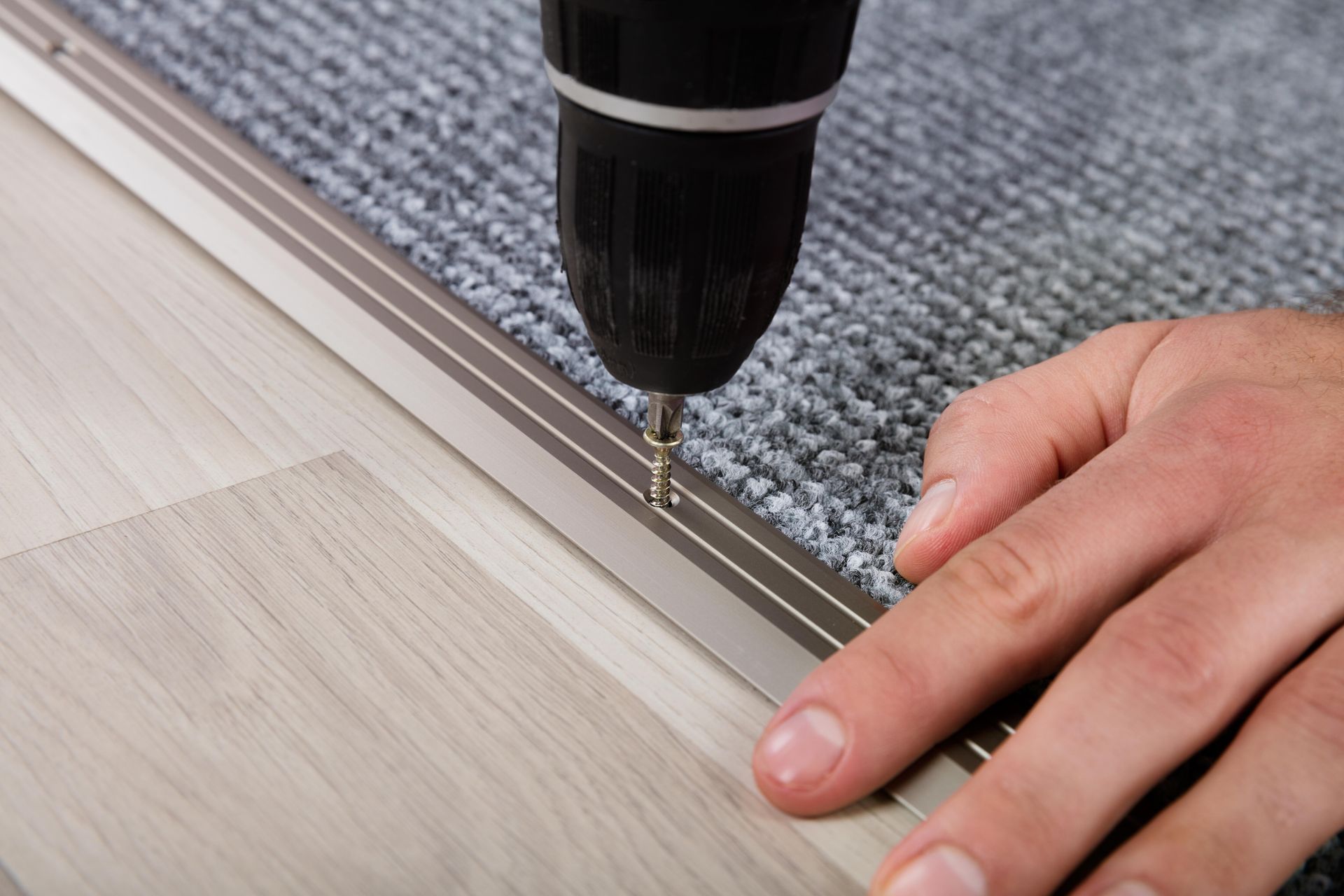 A person is using a drill to install a carpet on a wooden floor.