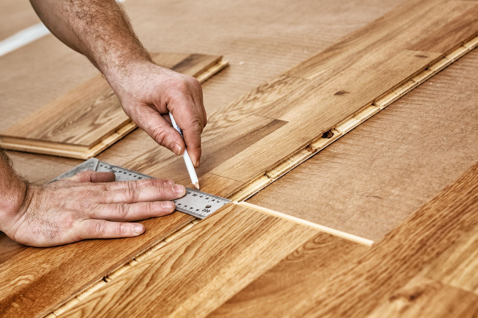 Hands measuring and marking a wood floorboard.