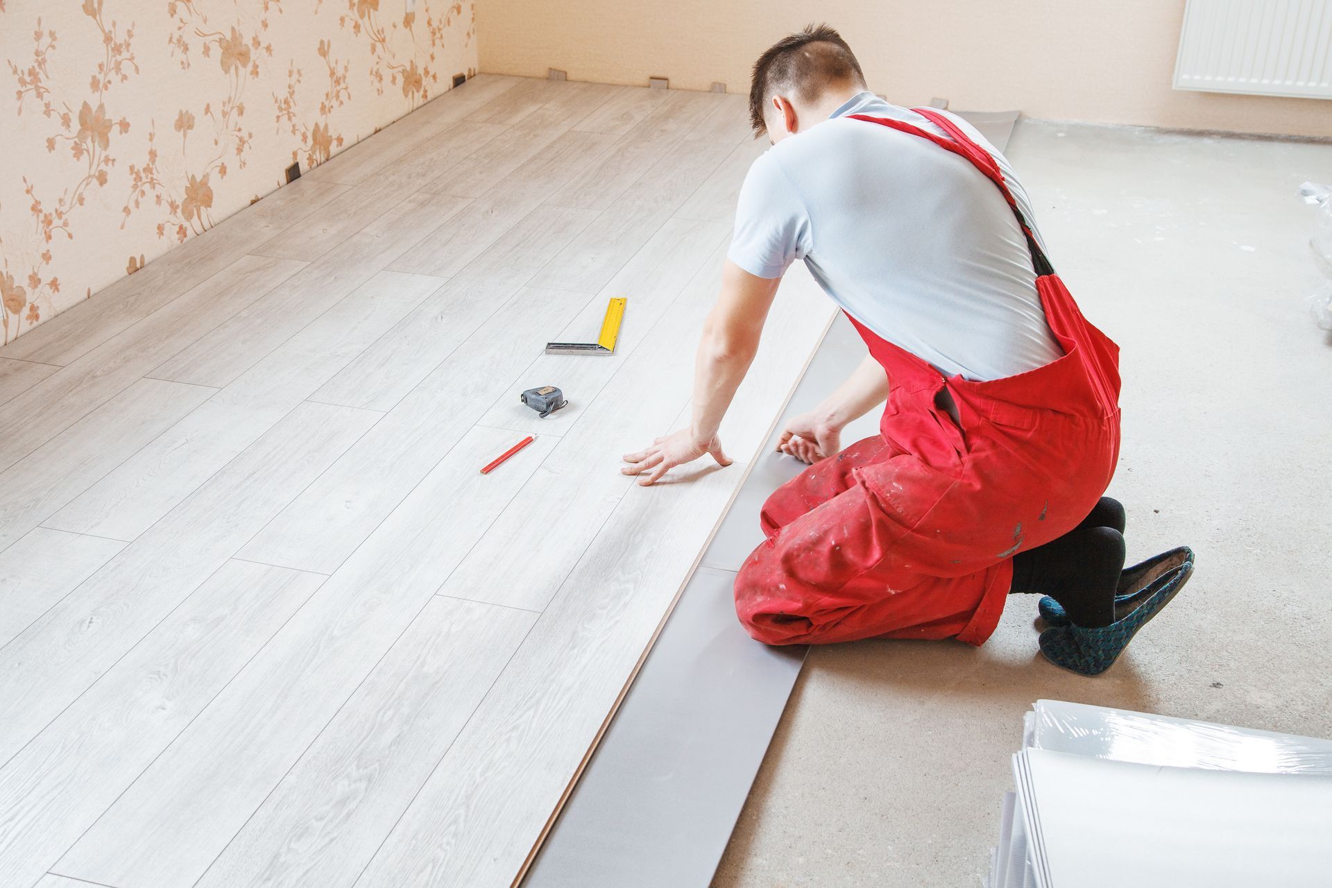 A man is kneeling on the floor while installing a wooden floor.