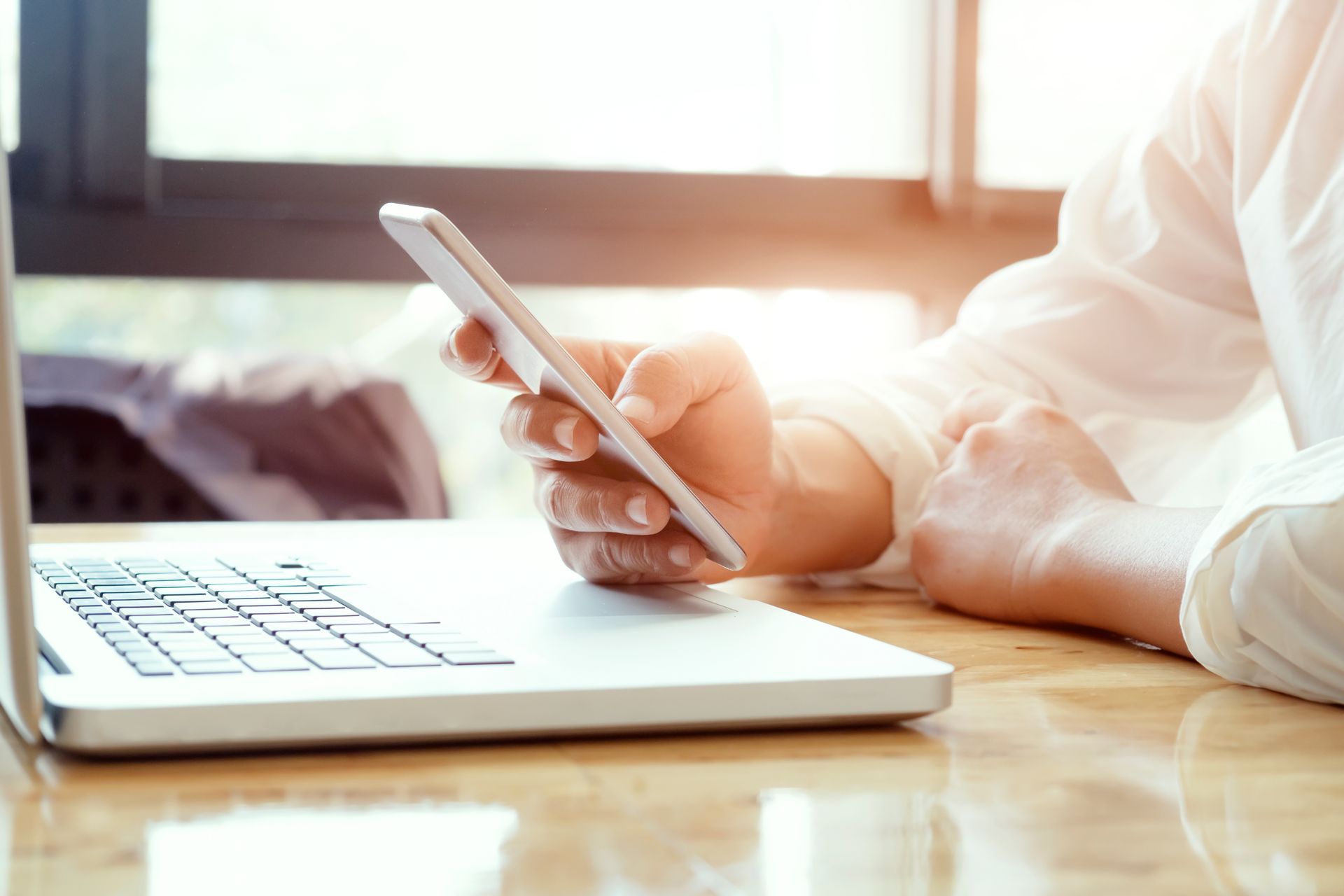 uma pessoa está sentada a uma mesa usando um laptop e um telefone celular.