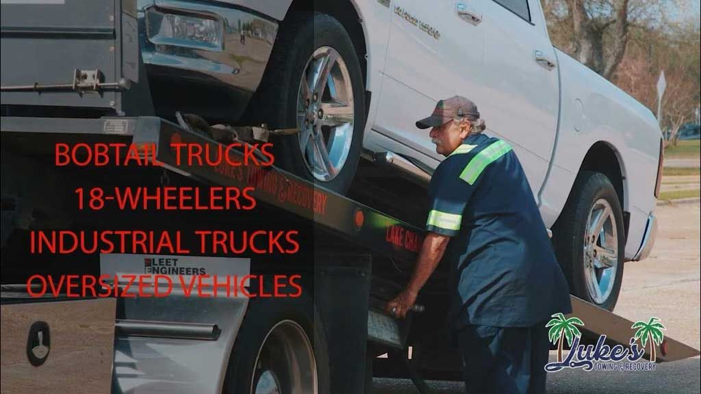 A man is loading a white truck onto a tow truck.