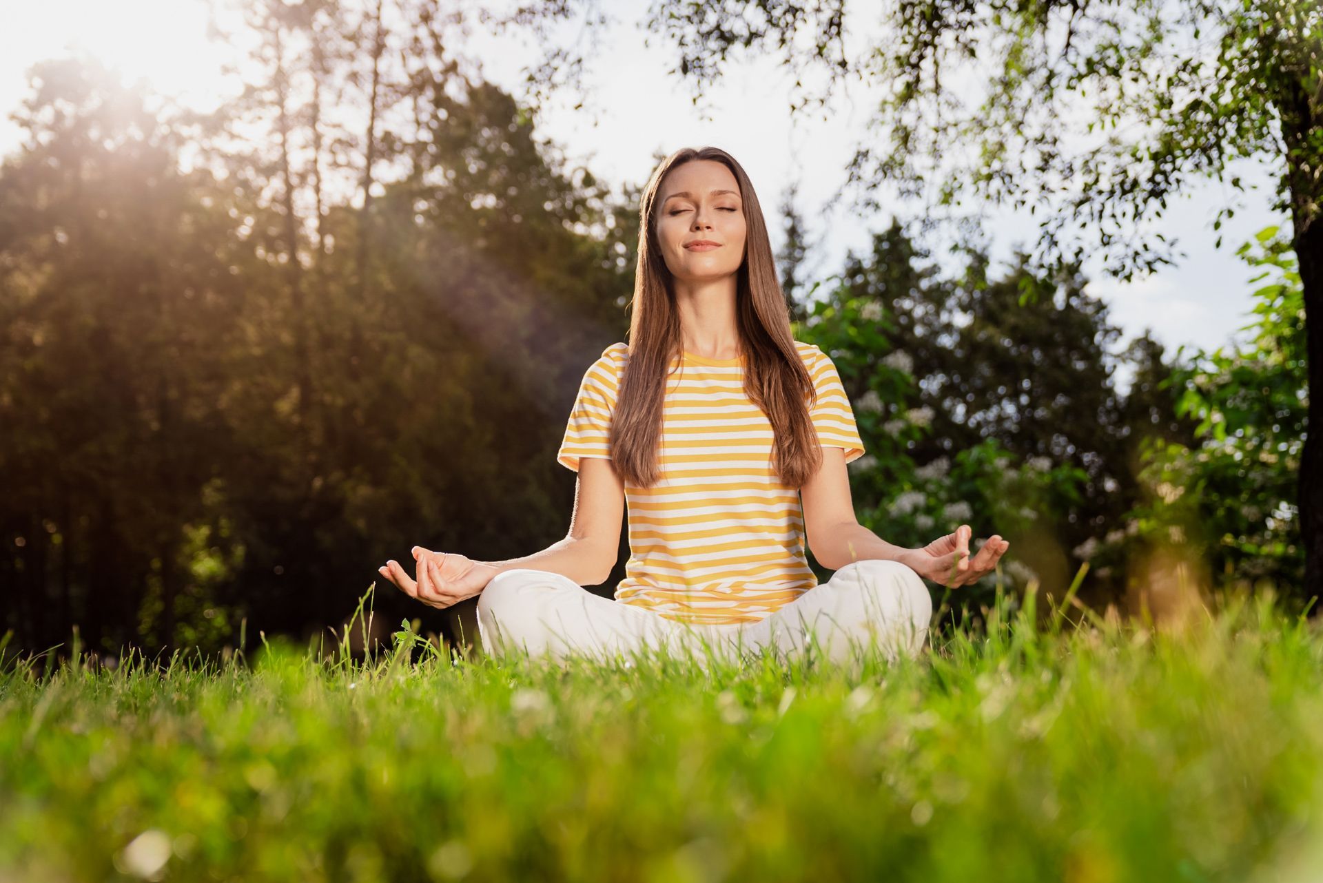 Woman meditating cross-legged in a sunny park, eyes closed, hands in prayer position