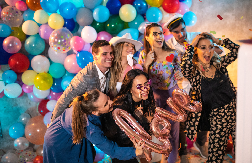 A picture of a bunch of people at a party taking a picture with balloons behind them.