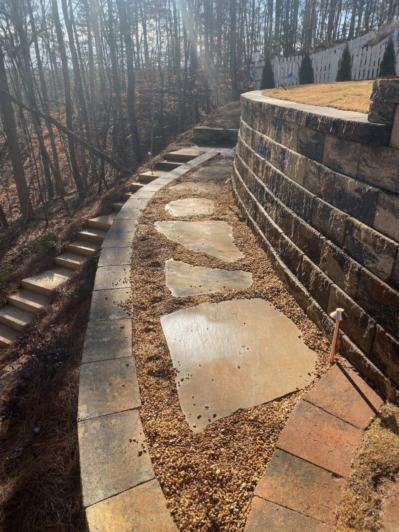 a stone walkway leading to a retaining wall in the woods .