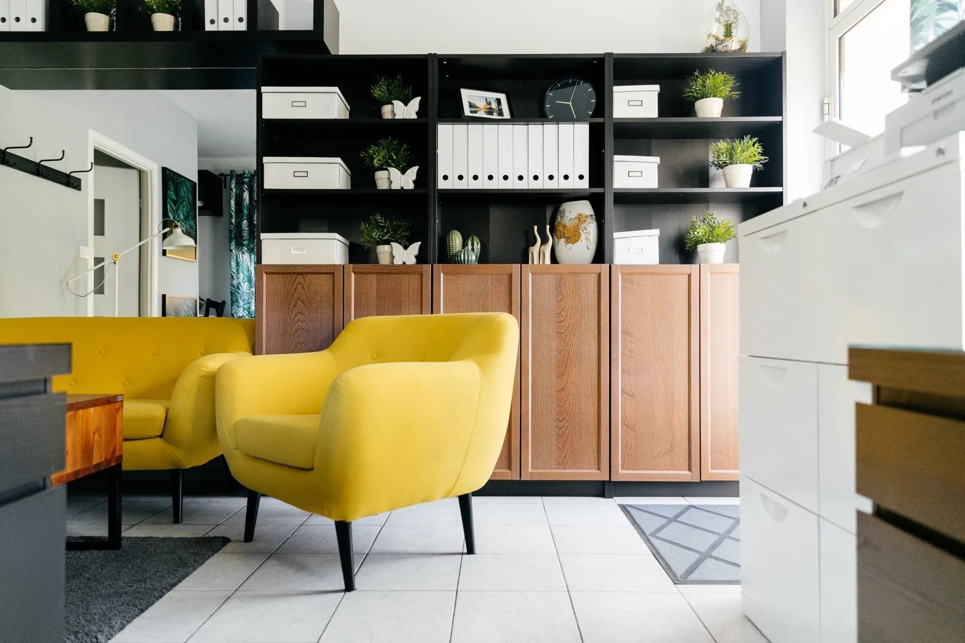 Bright modern kitchen with yellow chairs, black shelves, and white tile floor