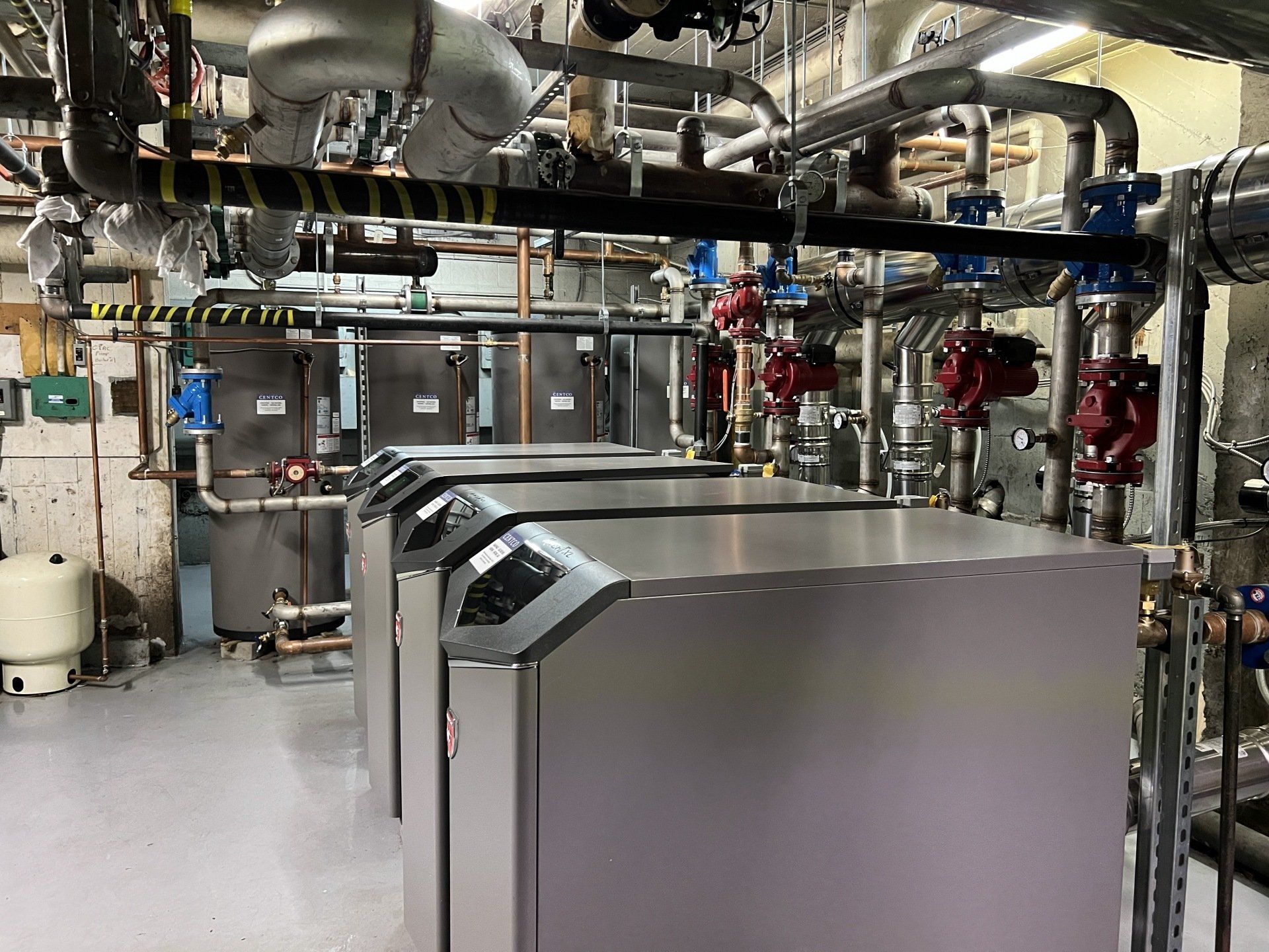 Une rangée de chaudières est alignée dans une pièce avec des tuyaux et des vannes.