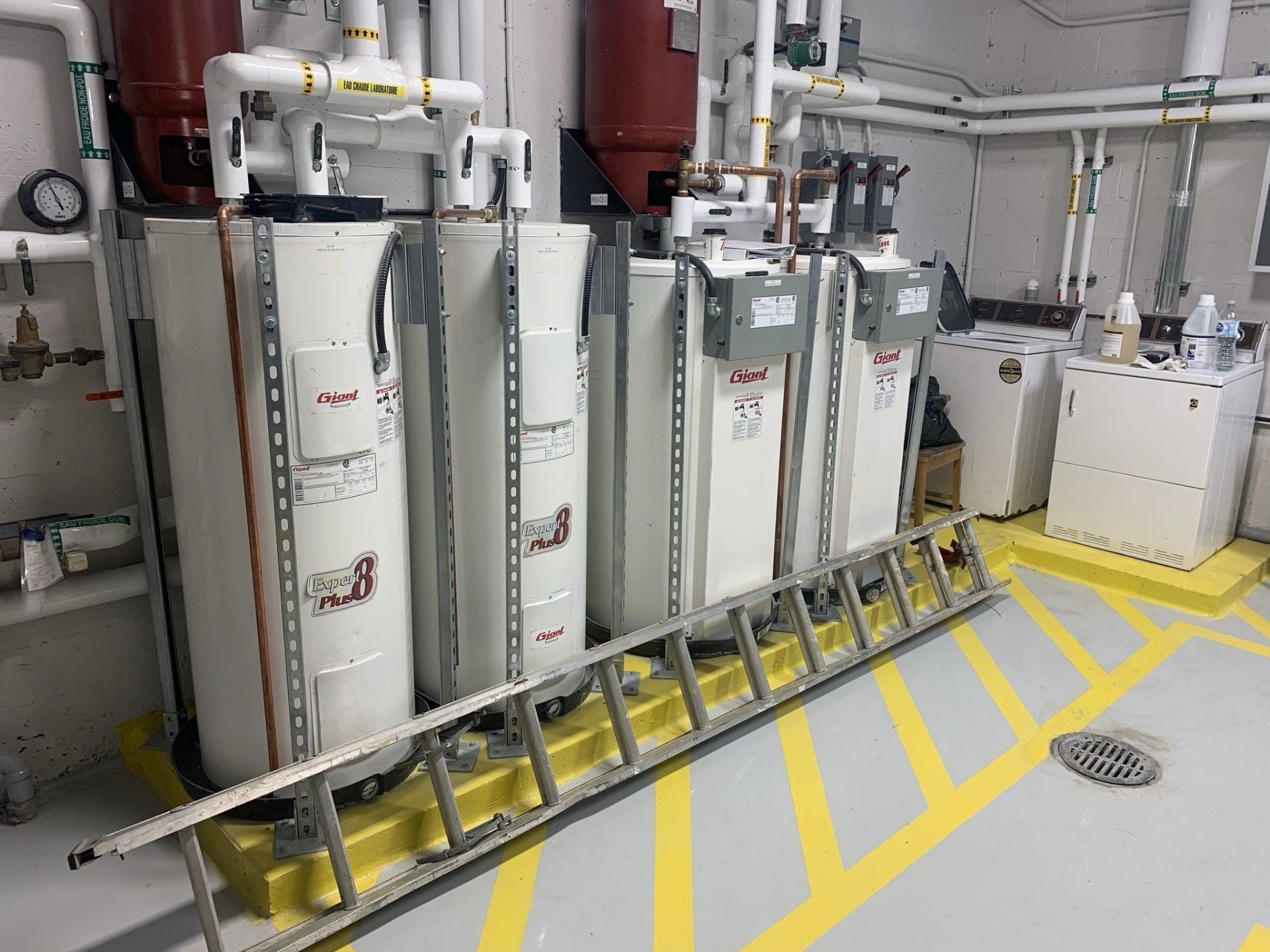 Une échelle est posée sur le sol à côté d'une rangée de chauffe-eau.