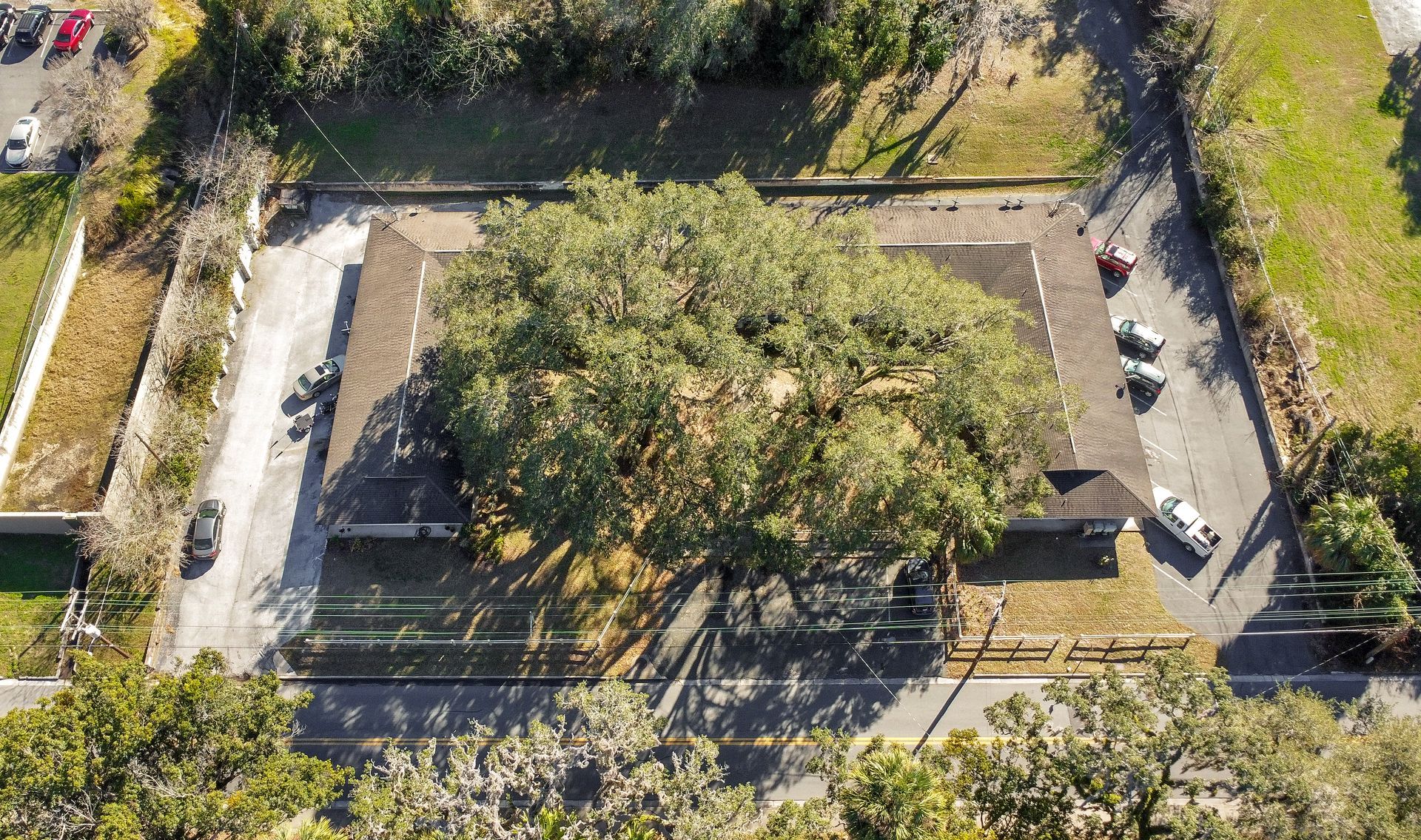 An aerial view of a house with a lot of trees and cars parked in front of it.