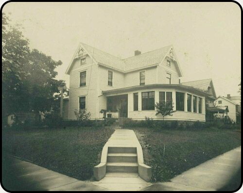 a black and white photo of a large white house with a porch .