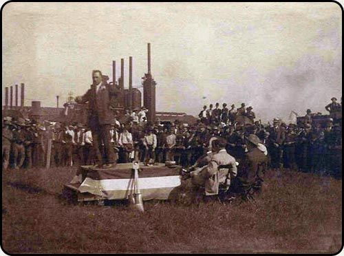 a man is giving a speech in front of a crowd of people in a field .