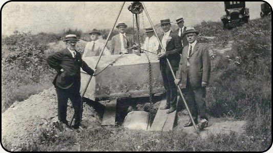 a group of men are standing around a coffin being lifted by a crane .