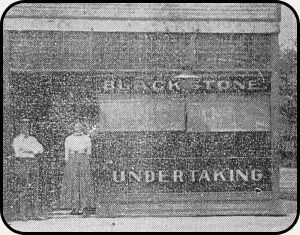 a black and white photo of two men standing in front of a building that says `` undertaking '' .