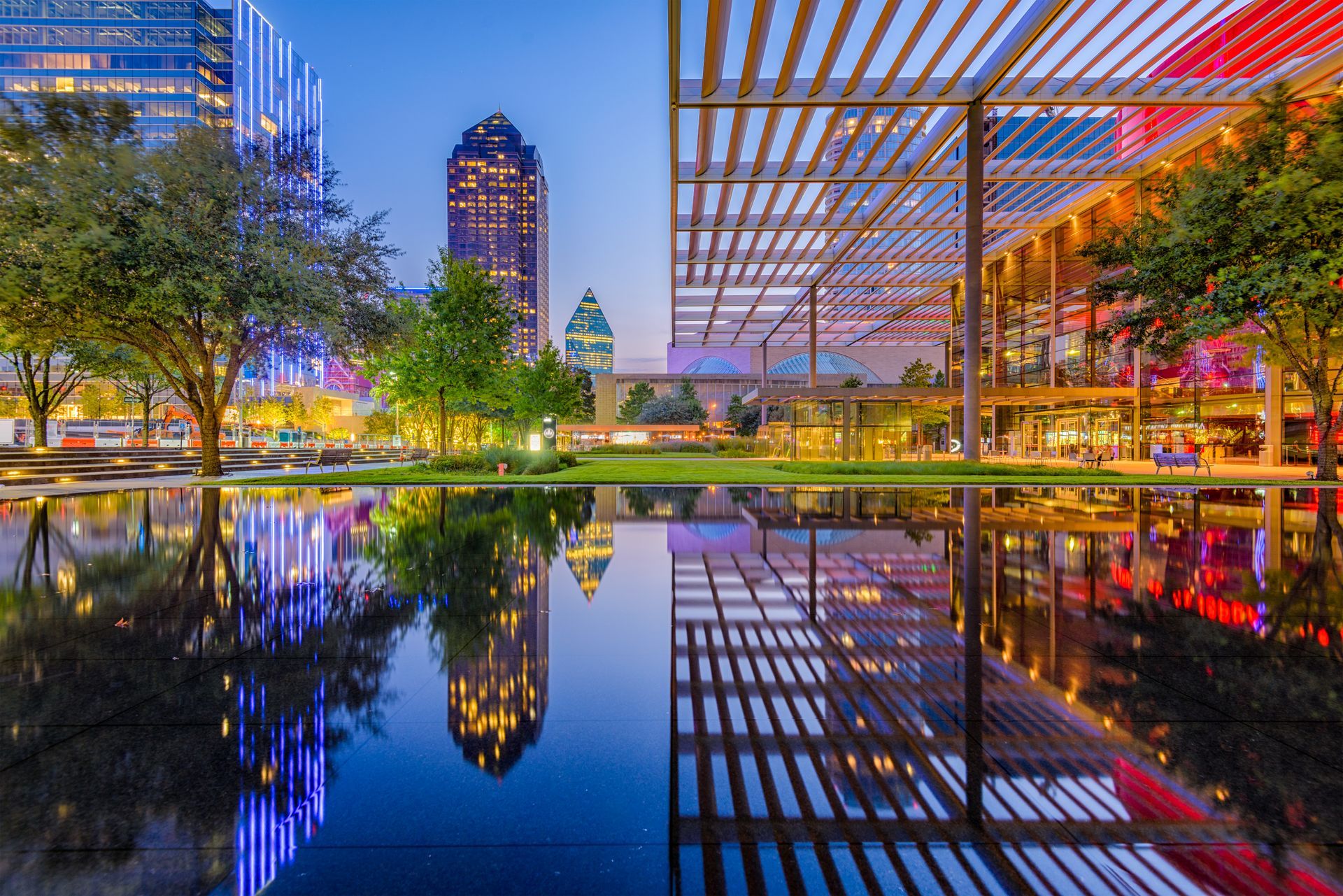 A city park with a pond and buildings reflected in the water at night.