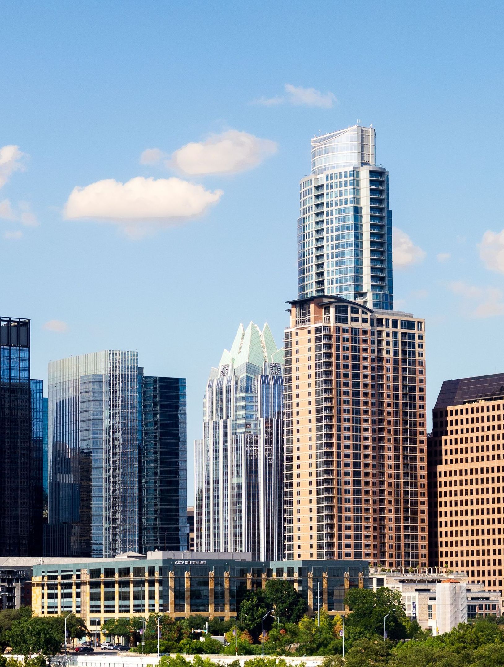 A city skyline with a lot of tall buildings and trees in the foreground