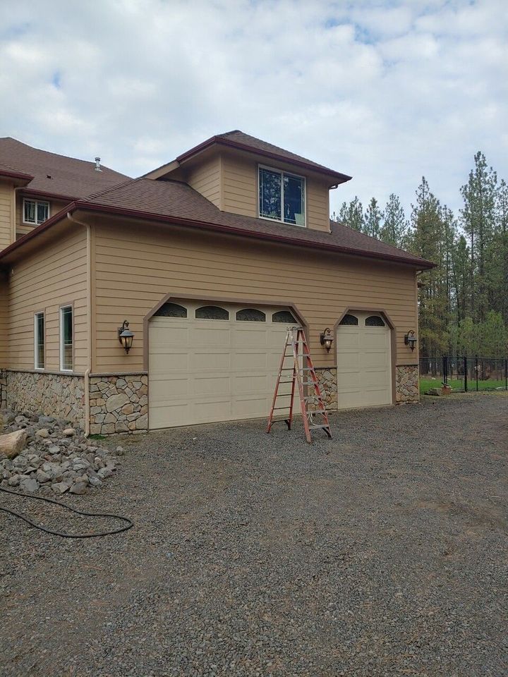 A large house with two garage doors and a ladder in front of it.