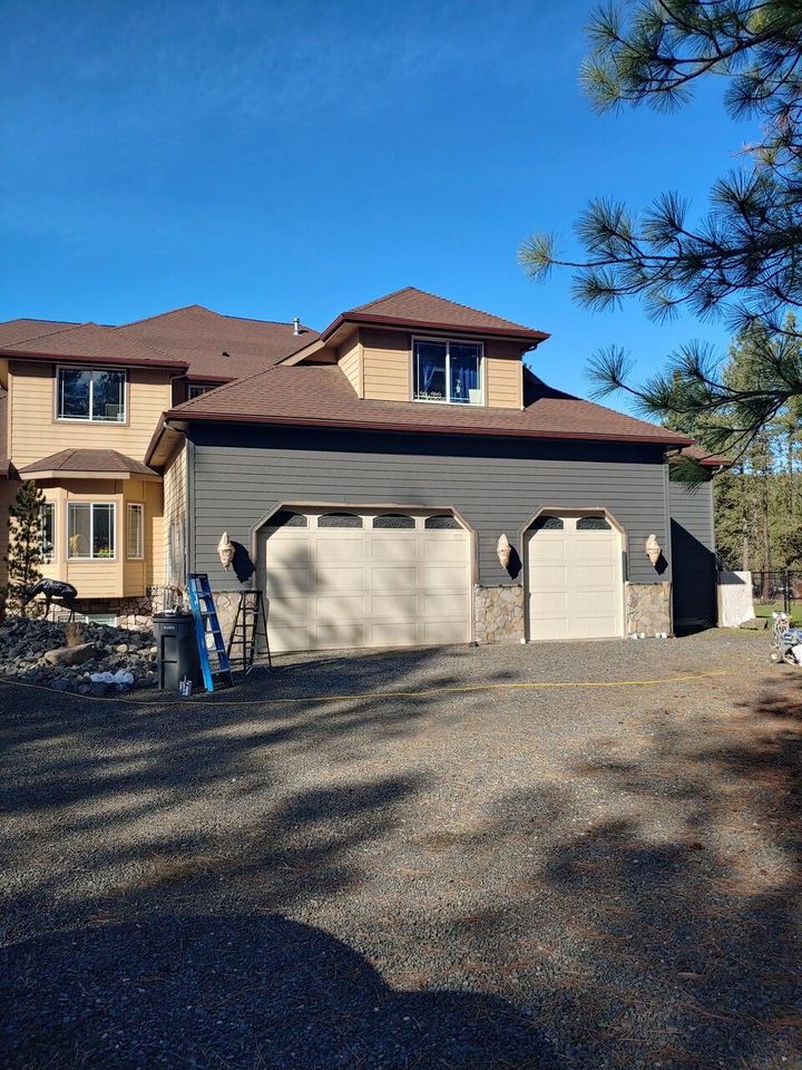 A large house with three garage doors is sitting on top of a dirt hill.