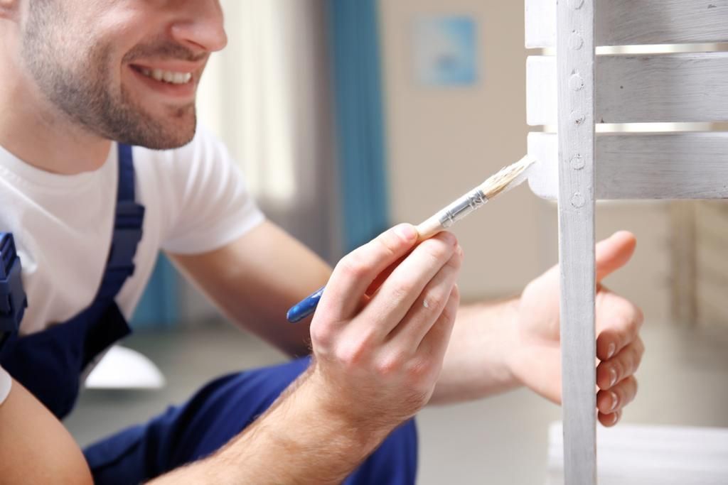 A man is painting a wooden shelf with a brush.