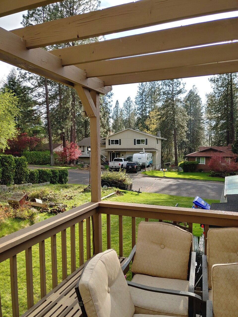 A deck with chairs and a pergola overlooking a house.