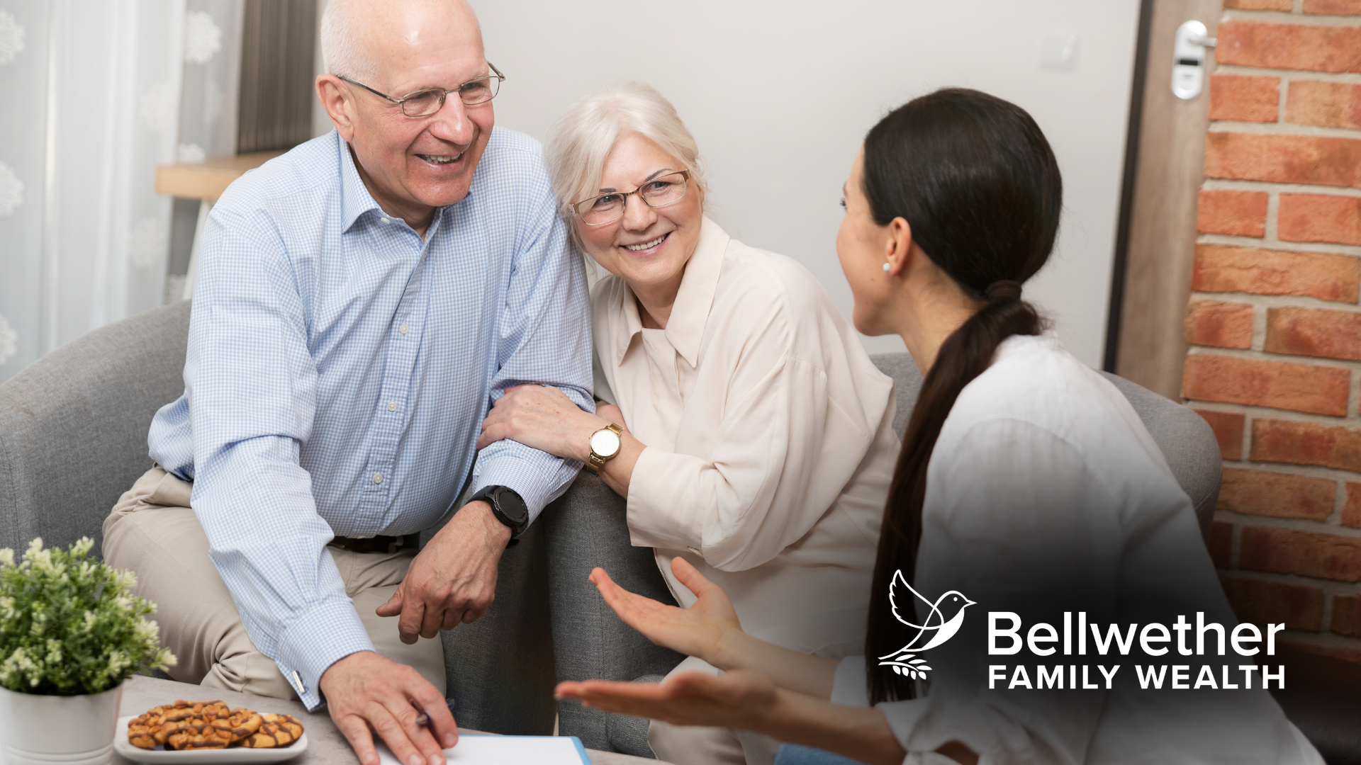 An elderly couple is sitting on a couch talking to a woman.