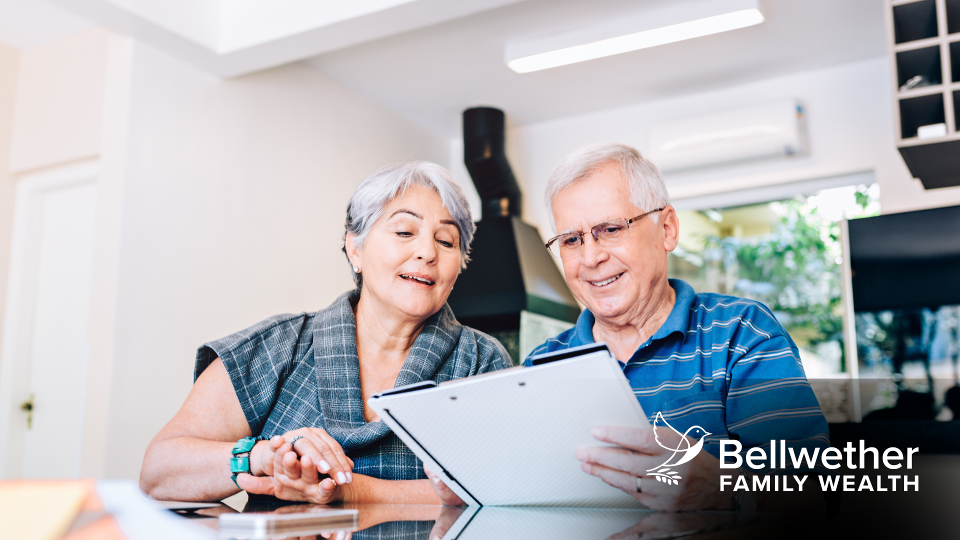 An elderly couple is sitting at a table looking at a clipboard.