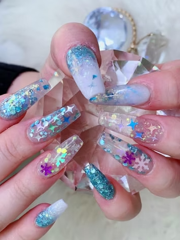 Long, sparkly blue and clear acrylic nails with winter-themed glitter and snowflake decorations.