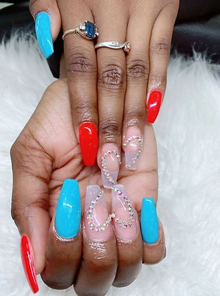 Hand with red, clear, and turquoise coffin-shaped nails, adorned with rhinestones, rings.