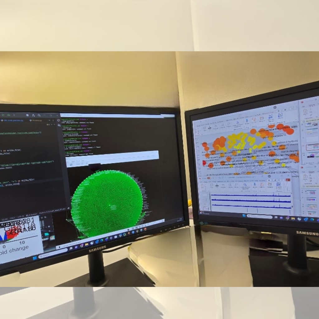 Two computer monitors show data visualizations: a circular green network graph on the left and a color-coded map on the right.