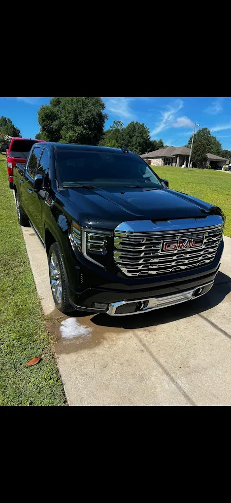Black GMC truck parked on a concrete driveway, with a red truck visible behind it.