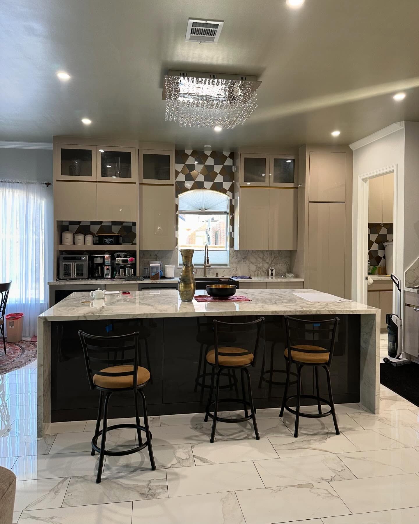 A kitchen with a large island , stools and a chandelier.