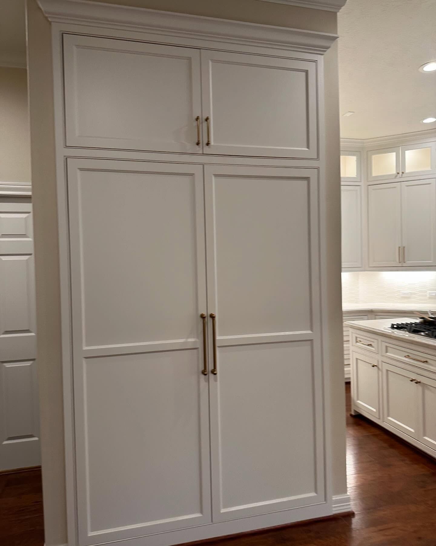 A kitchen with white cabinets and hardwood floors and a large white cabinet with two doors.