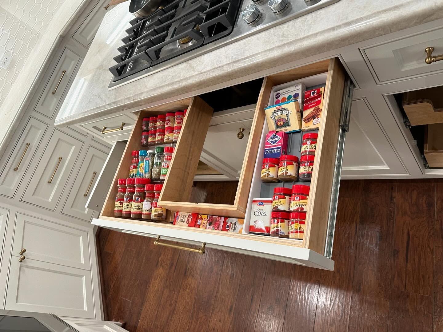 A kitchen with a stove top oven and a drawer filled with spices.