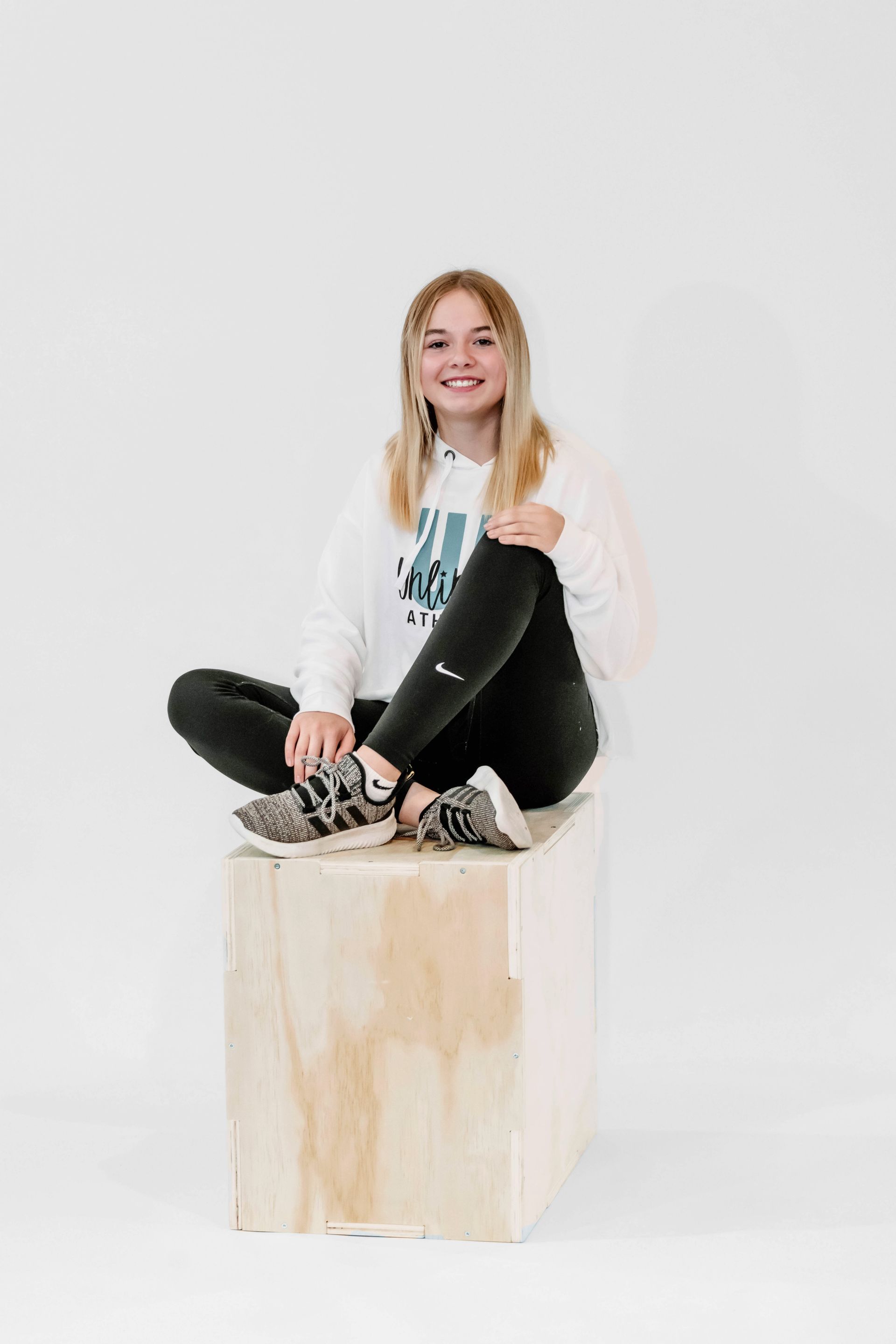 A young girl is sitting on a wooden box with her legs crossed.