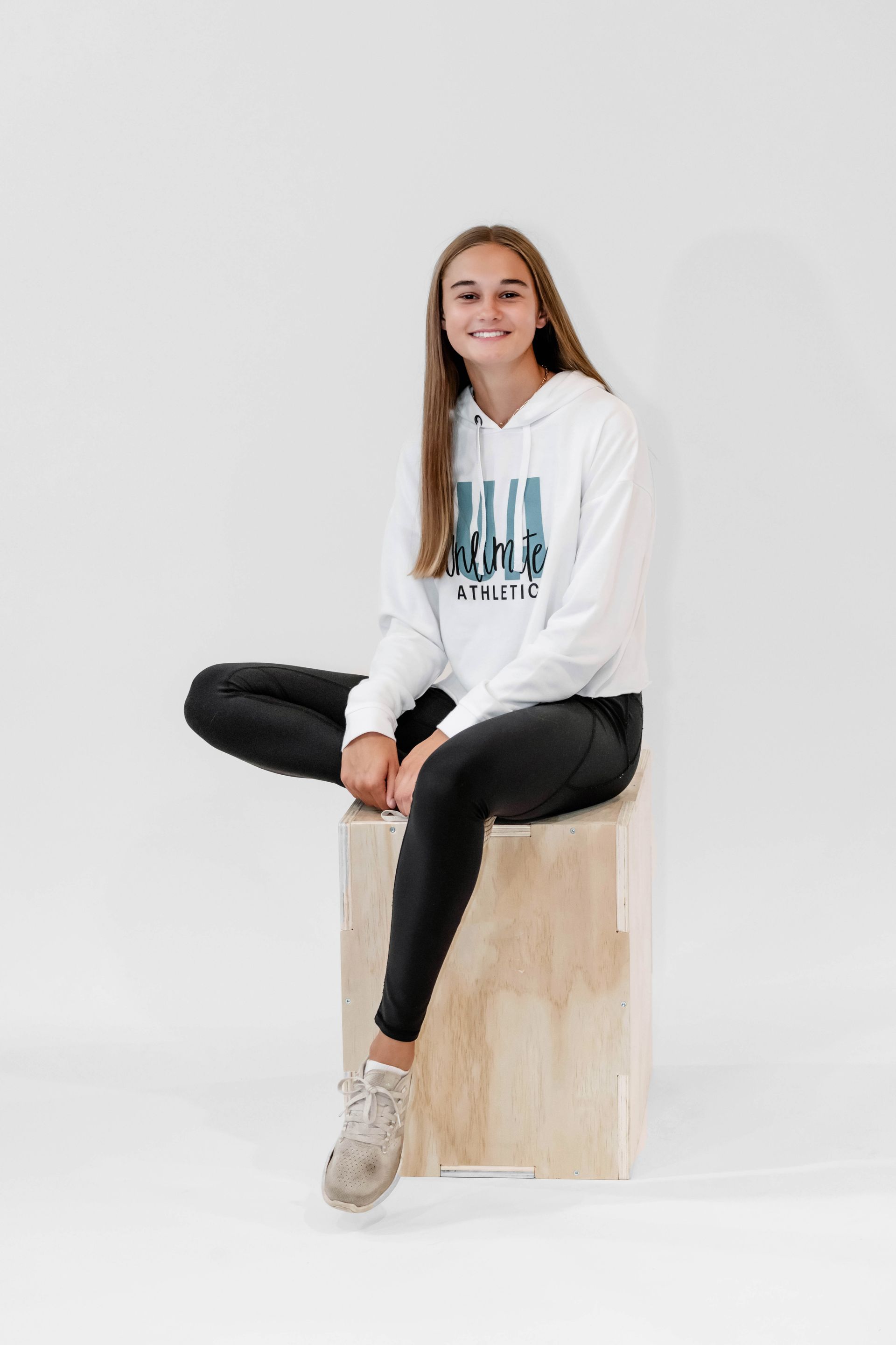 A young woman is sitting on a wooden box with her legs crossed.