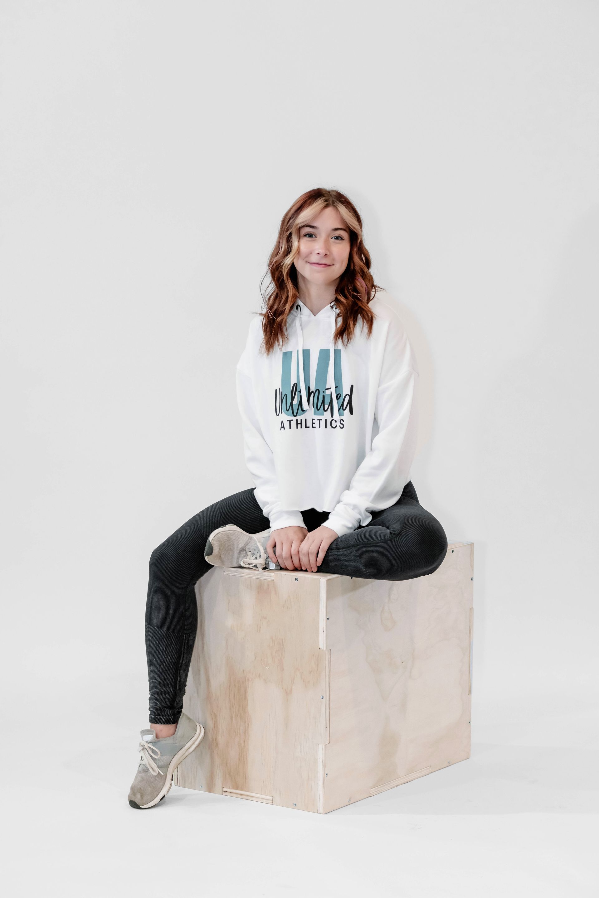 A woman in a white hoodie is sitting on a wooden box.