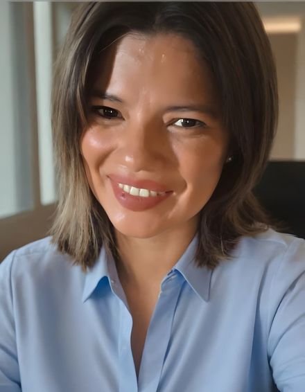 Una persona con el pelo hasta los hombros, que lleva una camisa azul claro con cuello, sonríe mientras mira a la cámara.