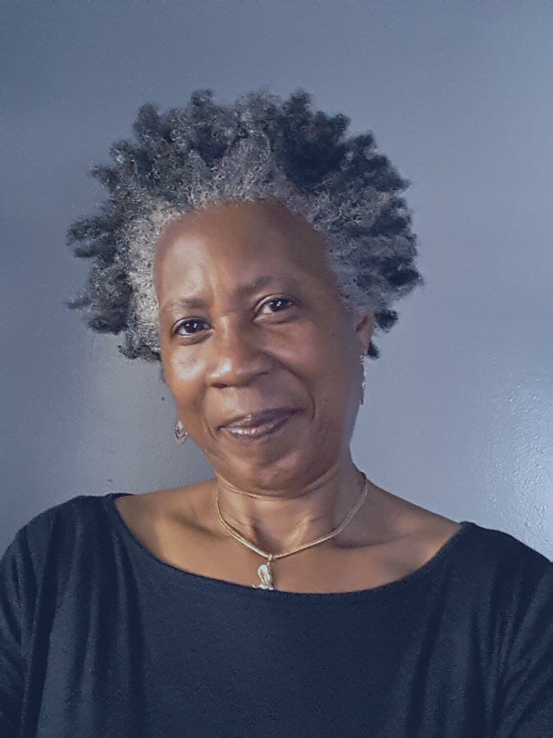 A woman with gray hair is wearing a black shirt and a necklace.