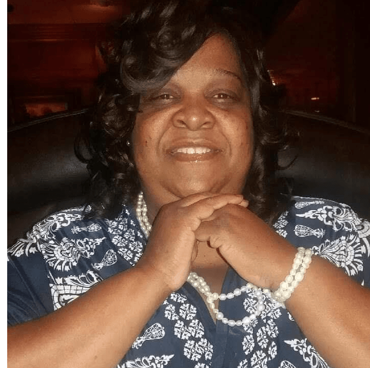 A woman wearing a blue shirt and pearls smiles for the camera